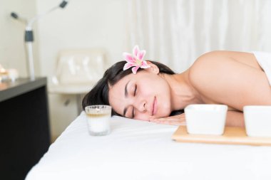 Rahatlamış, güzel, İspanyol bir kadın güzellik merkezinde kulağında çiçekle uyuyor.