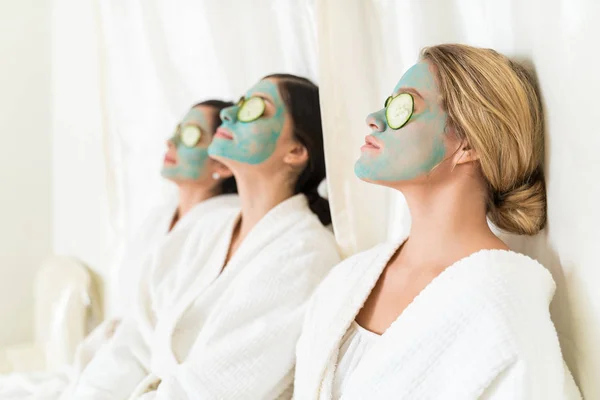 女性朋友放松与黄瓜和面罩 而坐在美容水疗中心 — 图库照片
