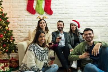 Gülümseyen erkekler ve kadınlar Noel partisinde oturma odasında kırmızı şarap içiyorlar.