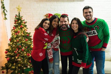 Mutlu erkek ve kadın arkadaşlar evde Noel kutlamaları eğlenirken çirkin kazak giyiyor