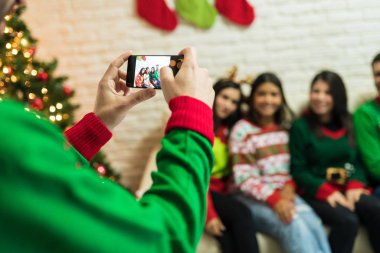 Evdeki Noel partisinde akıllı telefondan arkadaşlarını fotoğraflayan bir adam.