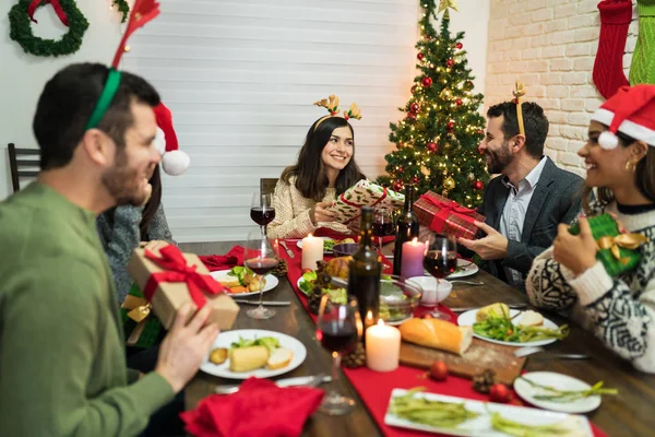 Amigos Sorridentes Trocando Presentes Sobre Mesa Jantar Casa Durante Natal — Fotografia de Stock