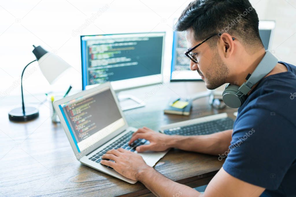 Side view of attractive Hispanic developer programming software using computer while working from home