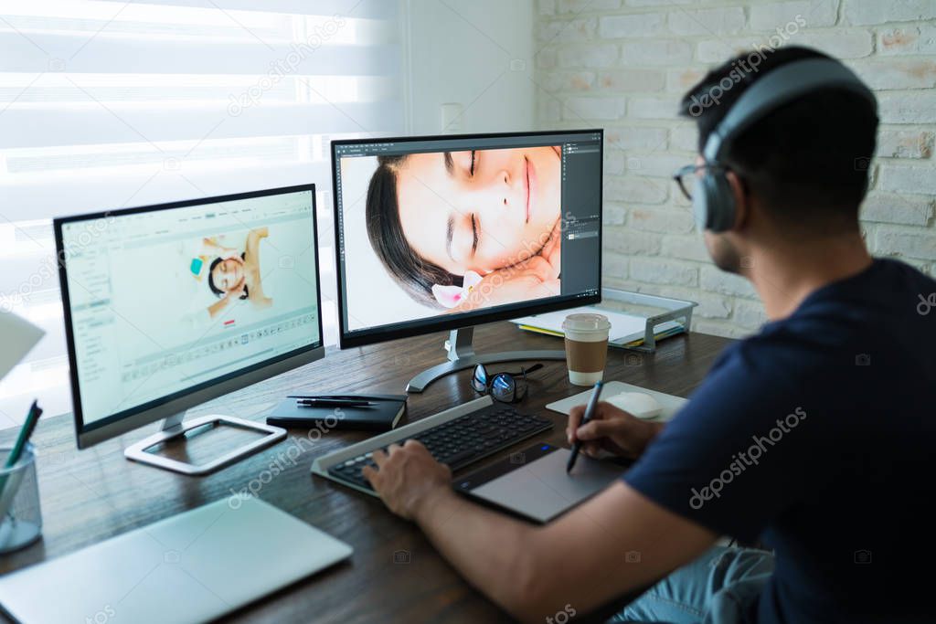 Male photographer wearing headphones while editing photos with graphic tablet at desk