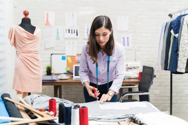 Kendine güvenen kadın terzi atölyede tezgahta makas kesiyor.