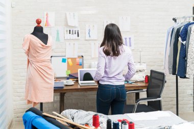 Tekstil endüstrisinde duvardaki tasarımları analiz eden genç terzinin arka görünüşü