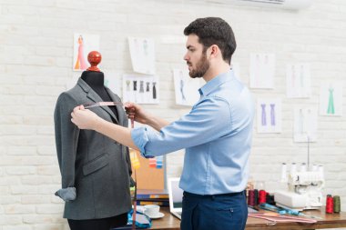 Yakışıklı terzinin atölyedeki bantla manken üzerinde ölçüm yaptığı yan manzara.