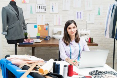 Tekstil atölyesinde çalışırken dizüstü bilgisayar kullanan güzel bir moda tasarımcısı