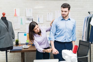 Female dressmaker taking measurements of male client in textile industry