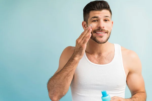 Sonriente Hombre Guapo Aplicando Crema Antienvejecimiento Mejilla Mientras Hace Contacto —  Fotos de Stock