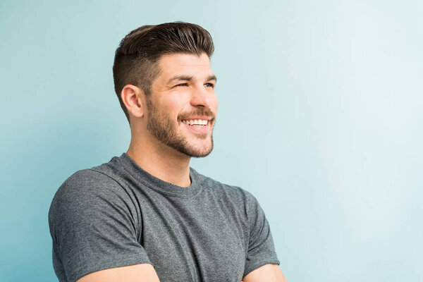 Closeup of smiling young man looking away while standing against turquoise background