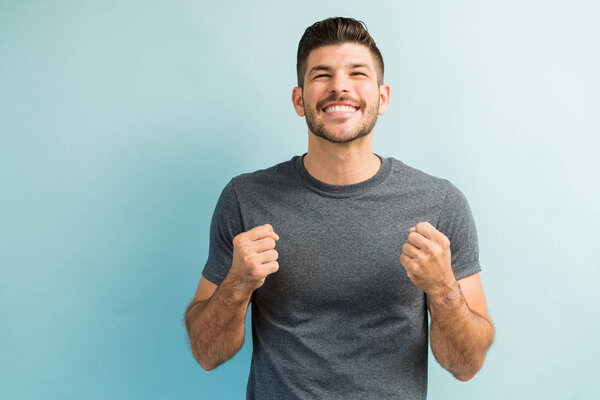 Young good looking male fan at cheering with fists while standing against plain background
