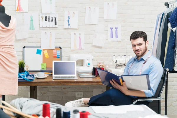 Atraente Alfaiate Masculino Analisando Seus Projetos Arquivo Enquanto Sentado Cadeira — Fotografia de Stock