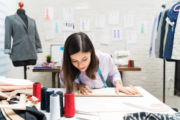 Schöne Weibliche Modedesignerin Zeichnet Muster Auf Werkbank Während Sie Bekleidungsstudio — Stockfoto