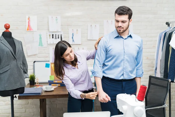 Female dressmaker taking measurements of male client in textile industry