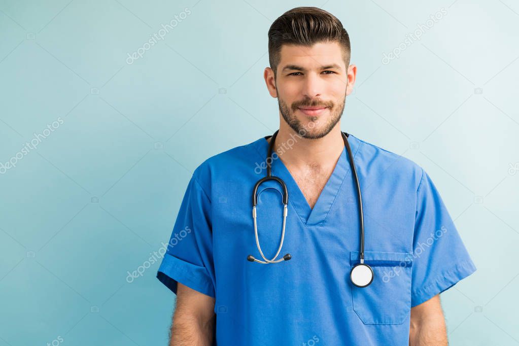 Handsome young surgeon with stethoscope around neck while making eye contact in studio