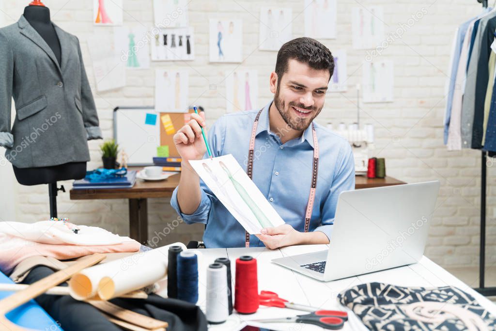 Smiling male tailor showing designs through video conference on laptop in textile industry