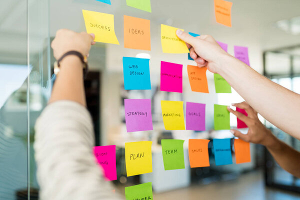 Business people arranging various adhesive notes with text on glass in office