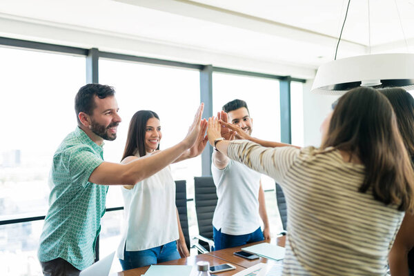 Латиноамериканская бизнес-команда дает друг другу пять в начале нового проекта на офисном совещании
