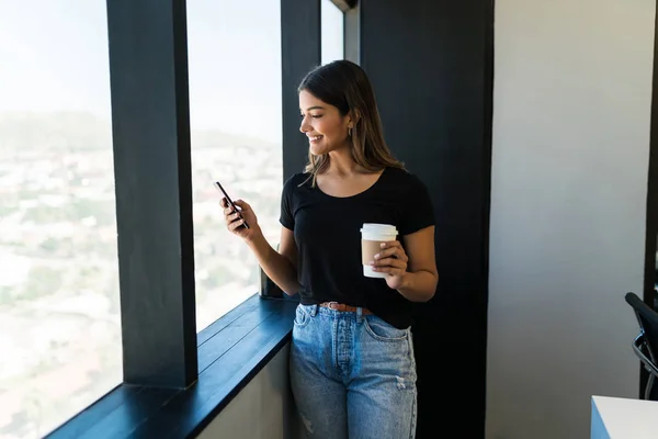 Ofiste Kahve Fincanı Tutarken Akıllı Telefon Kullanan Gülümseyen Kadın Yönetici — Stok fotoğraf