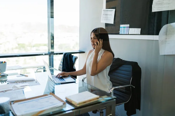 Beautiful young businesswoman on call through mobile phone while working in cubicle