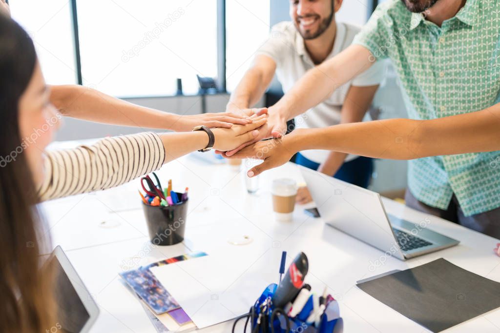 Cropped image of business team stacking hands over desk during meeting at office