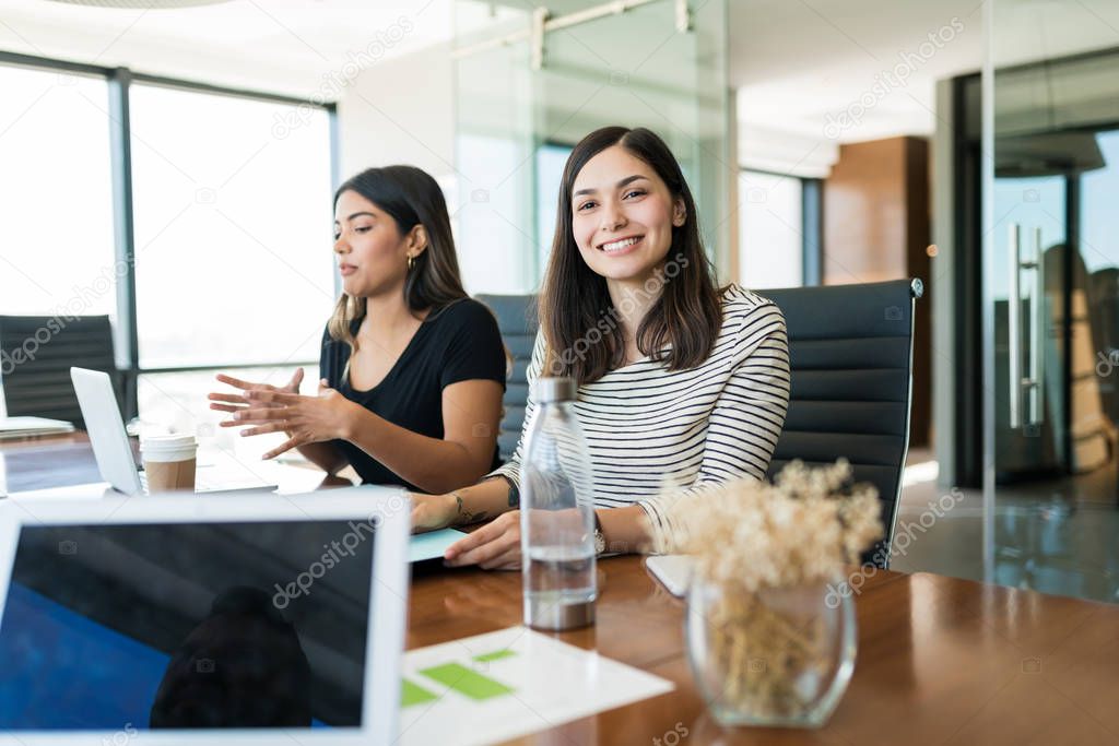 Portrait of smiling gorgeous businesswoman sitting with coworker during meeting in creative office