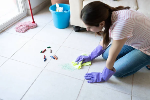 一名妇女戴着橡胶手套 在地板上擦拭乱糟糟的孩子留下的蜡笔污迹时的衣服 — 图库照片