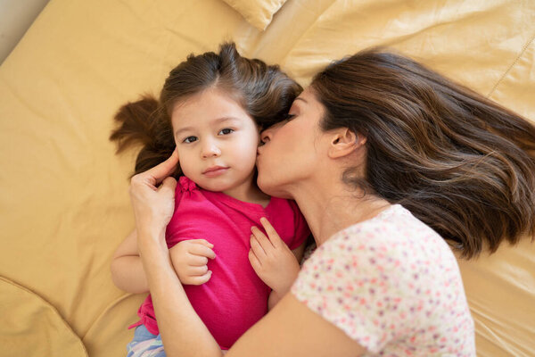 Portrait of a beautiful Caucasian woman in pajamas getting a kiss on the cheek from her mother in bed