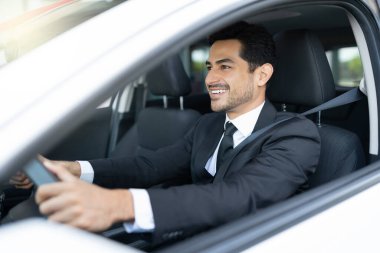 Gülümseyen Latin görünümlü iş adamı şehirde araba sürüyor.