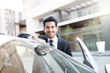 Kendine güvenen genç Latin iş adamının yeni arabası ile portresi