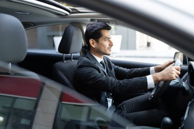 Kentte kendine güvenen genç Latin iş adamının araba sürüşünün yan görüntüsü