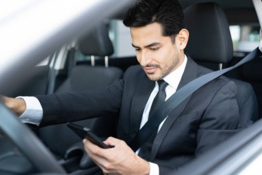 İspanyol genç işadamı şehirde araba kullanırken akıllı telefon kullanıyor.