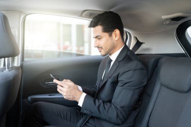 Latin genç iş adamının yan görüntüsü. Taksiyle seyahat ederken akıllı telefondan mesaj atıyor.