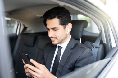 Yakışıklı Latin iş adamı arabayla seyahat ederken akıllı telefon kullanıyor.
