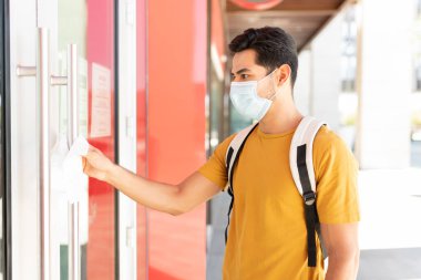 İspanyol genç adam koronavirüs salgını sırasında kapıyı açarken kağıt mendille dokunuyor.