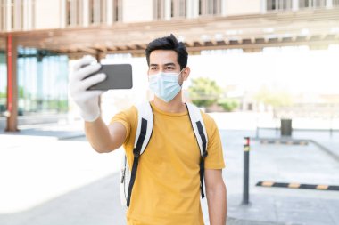 Latin genç adam COVID19 sırasında akıllı telefondan selfie çekiyor.