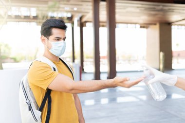 Latin genç adam COVID19 krizi sırasında el dezenfektanı kullanıyor.