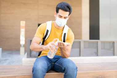 Kentte koltukta otururken dezenfekte eden İspanyol genç adam.