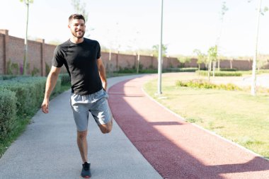 Yakışıklı Latin adam güneşli bir günde parkta yürüyüş yolunda geriniyor.