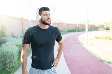 Atletik İspanyol genç adam parkta egzersiz yaparken kulaklıkla müzik dinliyor.