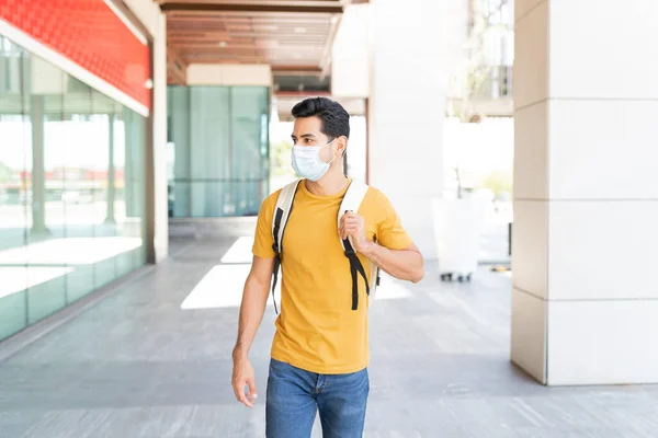 Latin young man with face mask walking on footpath in city during coronavirus outbreak