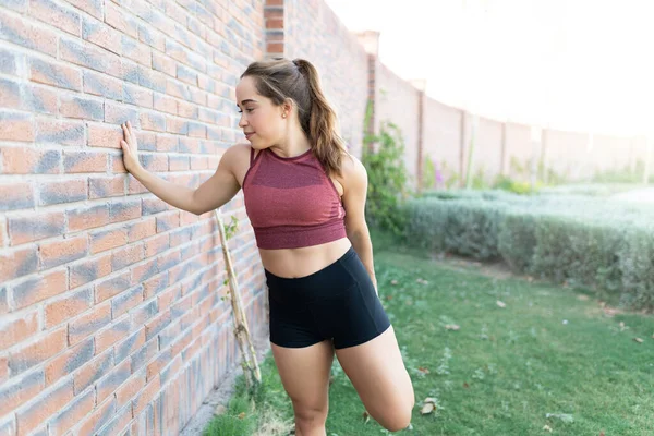 Beyaz bir kadın parkta tuğla duvarla egzersiz yapıyor.