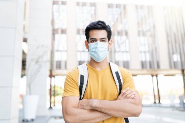 Kentteki koronavirüs salgını sırasında maske takan kolları çapraz duran kendinden emin genç bir adam.