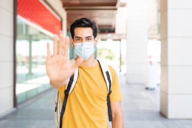 Koronavirüs salgını sırasında yüz maskesi takan Latin genç adam dur işareti yapıyor.