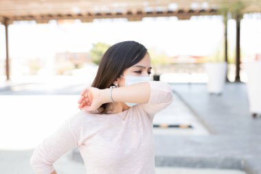 Coronavirüs salgını sırasında şehirde hapşırırken ağzını dirsekle kapatan kadın.