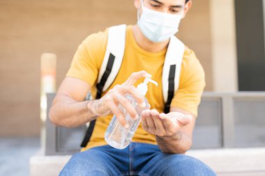 Latin delikanlının şehir merkezinde otururken elini dezenfektanla dezenfekte etmesi.