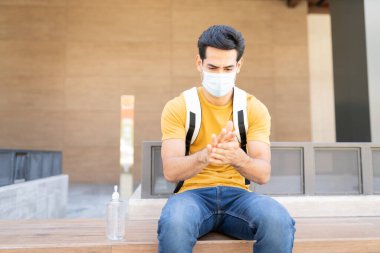 İspanyol genç adam Coronavirus krizi sırasında kentteki koltukta otururken dezenfektan sürüyor.