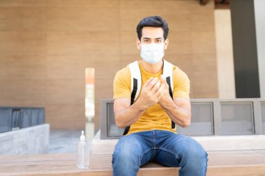 COVID19 salgını sırasında kentteki koltukta otururken elinde dezenfektan tutan Latin bir gencin portresi