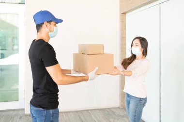 Teslimatçı kadın teslimatı yaparken sosyal mesafeyi koruyor ve güvenlik önlemleri alıyor.